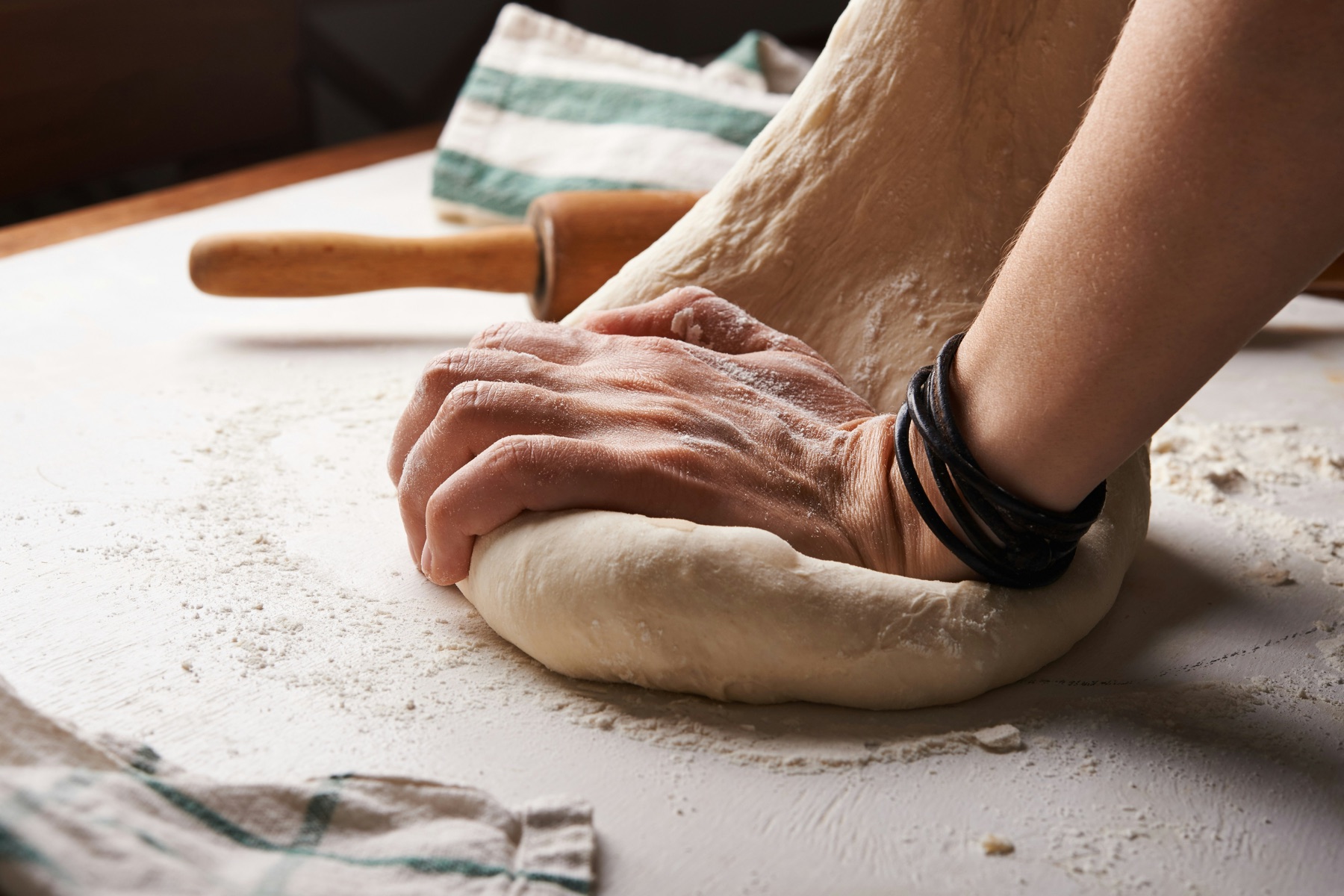 Hands mixing dough on a floured work surface